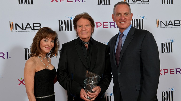 Caroline Beasley (Chairperson, BMI Board of Directors and CEO, Beasley Media Group) and Mike O’Neill (President & CEO, BMI) present John Fogerty with the BMI Board of Directors Award at the 73rd Annual BMI/NAB Dinner. Photo Credit- Lester Cohen for BMI.