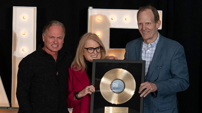 BMI’s Dan Spears and BMI songwriter Tim James presenting Rhode Hospitality Association CEO Dale Venturini with a BMI gold record at her retirement party held recently in Providence.